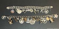 Two silver charm bracelets laid side by side on black background