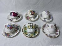 Front view showing six teacups upside down on matching saucers with floral patterns and gold trim.