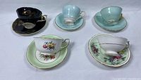 Displays five assorted teacups and saucers from above, showing various colors and floral designs.