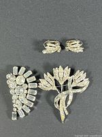 Top-down view of the set including two brooches and a pair of clip-on earrings displayed on a dark background