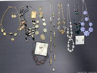 Full view of all necklaces and earring sets laid out on grey background, showing variety of styles, colors, materials including gold-tone, black, purple floral, green bead, and rhinestone.