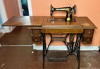 Full view of the vintage Singer sewing machine with its wooden cabinet and iron treadle pedal showing overall condition and layout.