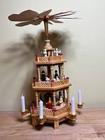 Front and side view of the wooden German Christmas pyramid showing three tiers with nativity and Christmas figurines, candle holders with white candles, and rotating propeller blades on top.
