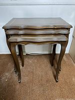 Set of 3 wooden nesting tables stacked together, showing front profile and legs. Dark brown finish, cabriole legs, scalloped edges visible.