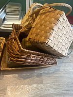Photo showing a stack of various wicker and woven wood baskets, with different shapes and weaves visible.