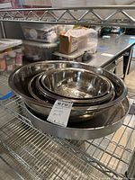 Stack of four nested stainless steel mixing bowls inside a round stainless steel cake pan on a wire rack shelf.
