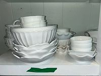 Stack of large to small white ceramic bowls with fluted and scalloped edges on a shelf