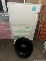 White wooden cabinet and black plastic cauldron grouped together against a wall.