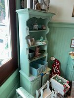Full view of light green wood cabinet with open top shelving and lower cabinet doors. Various decorative items displayed on shelves, not included with lot.