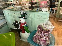 Front view of a painted wooden sideboard with drawers and doors, with a glass top. Various items and bags surround it.