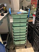 Front view of metal frame storage cart with eight green plastic drawers on wheels.