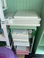 Stack of wooden cake pop holders and stands showing different sizes, mostly white with some green and pink holders, placed on shelves.