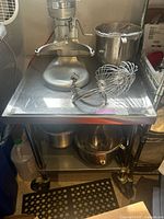 Full view of the stainless steel cart with heavy-duty casters, top flat surface, and lower storage shelf with some kitchen equipment placed on it.