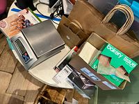 Photo showing MyWeigh digital scale, SentrySafe cash box, brown paper bags, bakery tissue, and flat glassine bags on a round table.