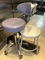Photo showing metal chair with vinyl cushioned round seat and backrest alongside a round metal stool with distressed white paint finish.