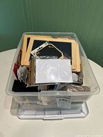 Plastic bin filled with multiple wooden-framed chalkboards and other miscellaneous stationery items including clothespins and tags.