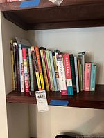 Photo shows bookshelf with 15 baking and dessert cookbooks including Hello, Cupcake!, Cake Balls, Cake Pops, and others arranged upright.