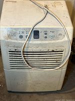 Front view of white portable dehumidifier with visible dirt marks, power cord placed on top.