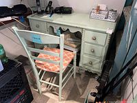 Photo of painted wooden desk with five drawers and brass knobs, light green with chips in paint.