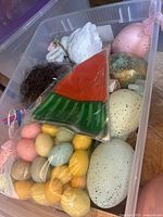 Plastic bin containing assorted pastel colored plastic eggs, large ceramic speckled eggs in cream, blue and green with gold glimmer, and watermelon slice decoration.