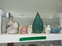 Front view of seven ceramic bird figurines showing various colors and sizes on a white shelf.