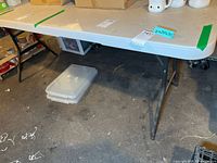 Full view of LifeTime 6-foot folding table set up in basement environment showing legs, frame, and tabletop with green tape markings.