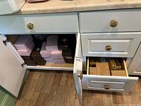 View of an open cabinet with multiple pink and white striped boxes, dark brown boxes stacked inside, and cardboard food boxes in drawers.