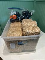 Clear plastic bin containing three straw bales and multiple plastic Halloween themed containers in resealable plastic bags.