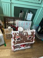 Wide view showing two gingerbread house figurines with candy and frosting details, Christmas-themed framed wall art behind, and part of the red metal truck visible.