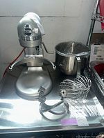 Front view of silver mixer with bowl and attachments on stainless steel cart