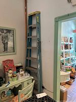 Full view of blue Werner metal extension ladder standing against wall, folded up, showing yellow end caps on top and several metal steps.