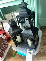 Set of three black decorative lanterns with battery operated candles placed on a plastic storage bin, showing overall condition and detail.
