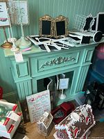 Photo of painted wooden fireplace mantel in teal green with various decorative items on top and front panel showing ornate carved detailing.
