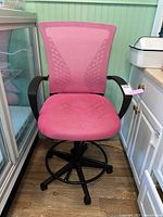 Front view of the pink office chair showing the upholstered seat with visible stains, armrests, and the wheel base.