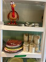 Wide view of shelf showing plastic turkey figurine, metal car lids, painted Ball canning jars, and colorful plates.
