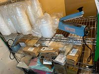 Impulse sealer and assorted plastic bags and food containers arranged on metal shelving unit.