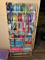 Front view of wooden ribbon storage rack filled with multiple colorful ribbon spools organized on dowels.