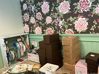 Wide view of assorted boxes stacked on a desk near floral wallpaper and green wainscot paneling.