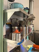 Photo showing two large stainless steel shelves mounted on wall with kitchen utensils and containers placed on them.