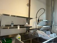 Four stainless steel wall-mounted shelves installed above a kitchen sink area with some cleaning supplies present on lower shelves.