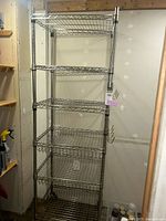 Full view of the metal wire shelving unit against a wall with five wire mesh shelves and caster wheels.