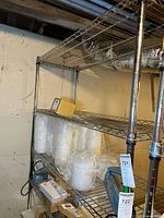 Full view of wire shelving unit including bottom three shelves with various stored items such as plastic cups and boxes.