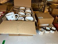 Box with multiple ceramic mugs including white snowman face mugs and other animal shape mugs packed in cardboard compartments