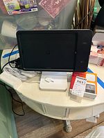 Photo showing black tablet in stand on table with white cables and Square Reader box and stand.