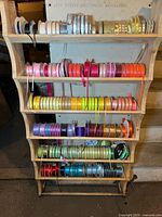 Full view of wooden storage unit filled with colorful ribbon spools displayed on five shelves