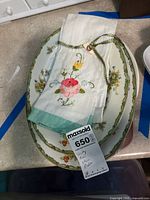 Porcelain serving plates with floral borders and folded embroidered napkins on top showing floral embroidery and green trim.