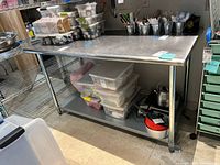 Front angle view of the stainless steel kitchen work table showing surface condition and items stored under the lower shelf