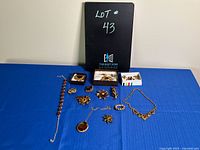 Full view of jewelry lot number 43 laid out on blue cloth including multiple amber coloured jewelry pieces such as necklaces, brooches, and bracelets.