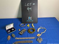 Full view of lot on blue cloth including earrings, bracelets, brooches, cufflinks, necklace, and box with lot number board