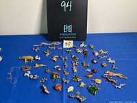Table display of approximately 50 animal brooches and pins arranged on a blue fabric surface with a black sign marked “94” behind